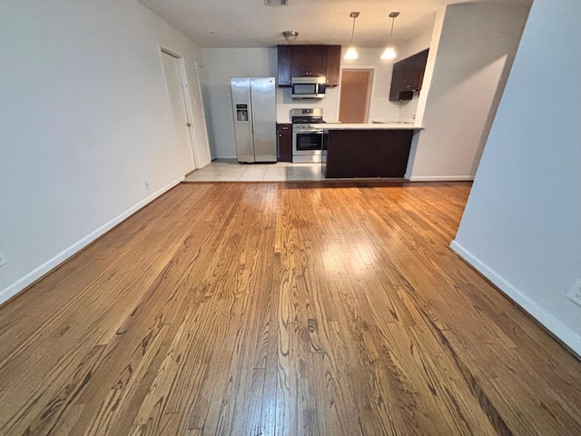 kitchen featuring decorative light fixtures, wood finished floors, appliances with stainless steel finishes, light countertops, and baseboards