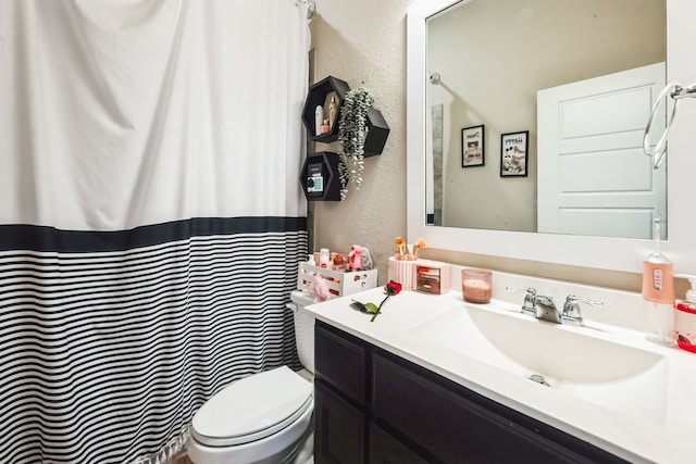 full bathroom with toilet, vanity, and a textured wall