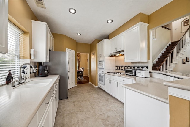 kitchen featuring white appliances, a sink, decorative backsplash, under cabinet range hood, and white cabinetry