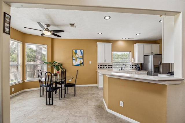 kitchen featuring visible vents, light countertops, stainless steel refrigerator with ice dispenser, white cabinetry, and a sink