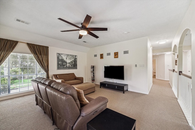 living area with visible vents, light carpet, arched walkways, and a ceiling fan