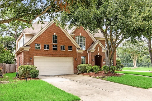 traditional-style home featuring a front yard, concrete driveway, fence, and brick siding