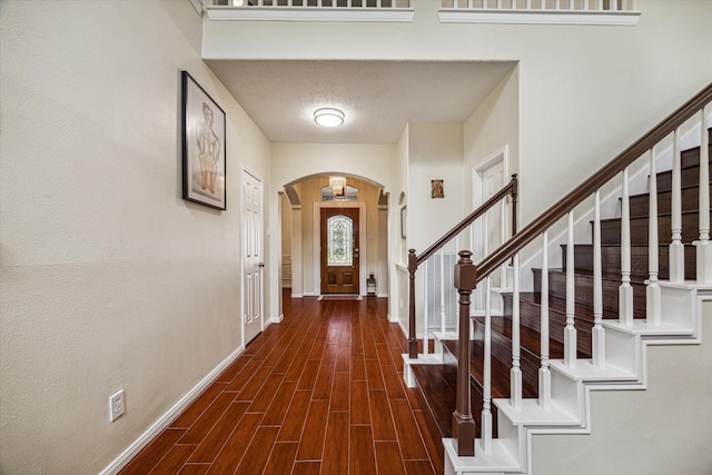 entrance foyer with a textured ceiling, dark wood finished floors, arched walkways, baseboards, and stairs