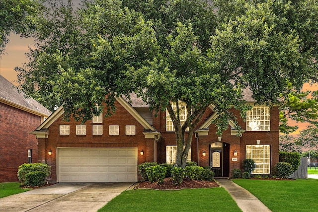 view of front of property featuring brick siding, a lawn, an attached garage, and driveway