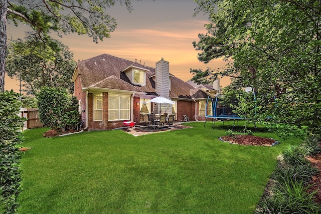 rear view of house featuring brick siding, a patio area, a trampoline, and fence