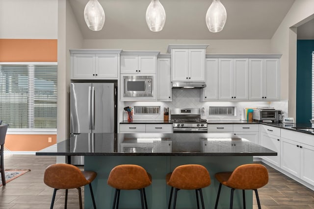 kitchen with under cabinet range hood, backsplash, dark wood finished floors, white cabinetry, and stainless steel appliances