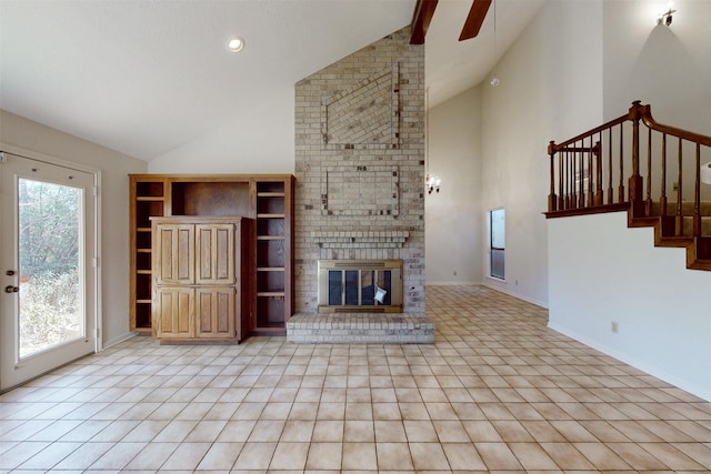 unfurnished living room featuring a brick fireplace, baseboards, ceiling fan, stairs, and high vaulted ceiling