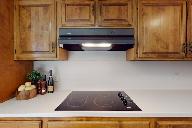 kitchen with light countertops, black electric cooktop, brown cabinetry, and under cabinet range hood