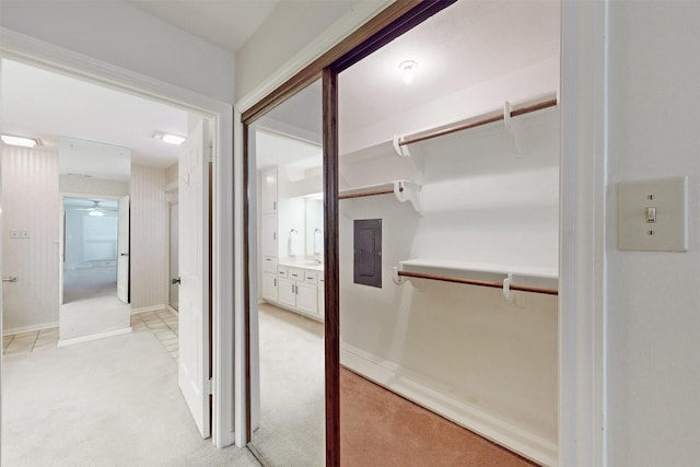 hallway featuring electric panel, baseboards, and light colored carpet