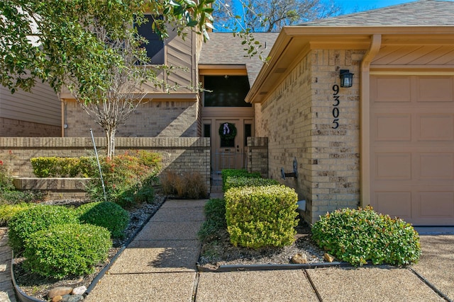 view of exterior entry with a garage, brick siding, and roof with shingles