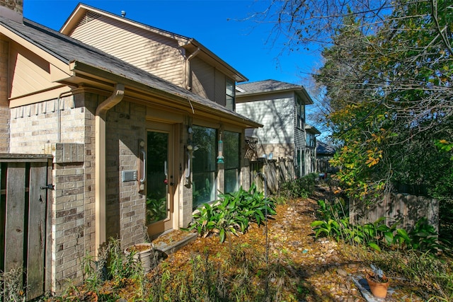 view of exterior entry featuring fence and brick siding