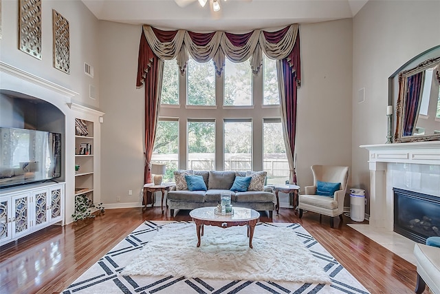 living room featuring a premium fireplace, a high ceiling, visible vents, and wood finished floors