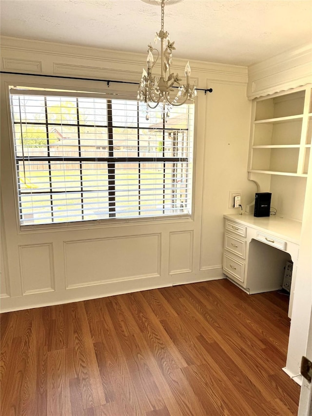 unfurnished dining area featuring a notable chandelier, a healthy amount of sunlight, wood finished floors, and built in desk