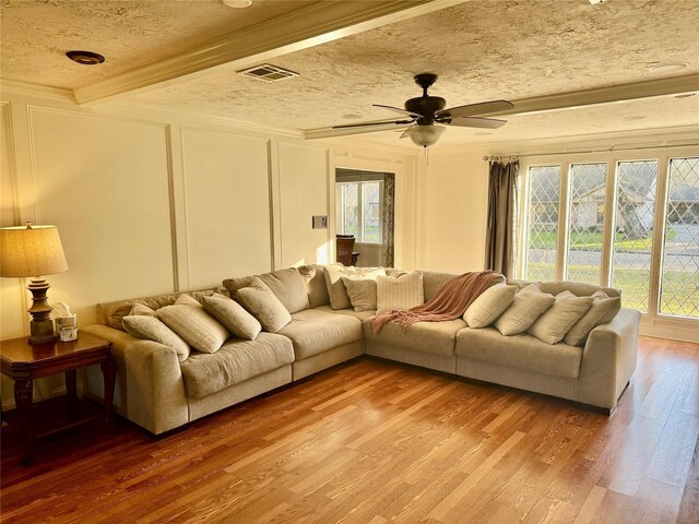 living room featuring a wealth of natural light, a decorative wall, visible vents, and light wood finished floors