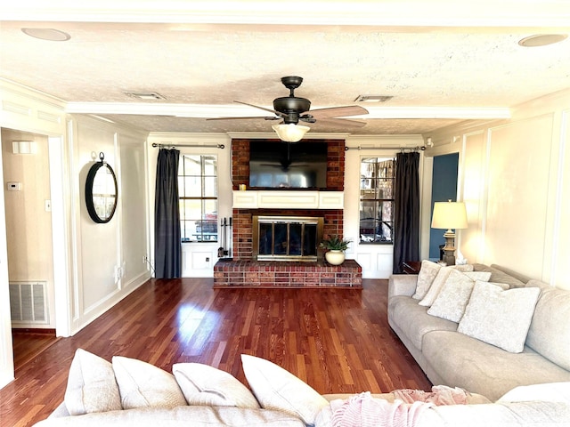 living area with crown molding, wood finished floors, a fireplace, and visible vents