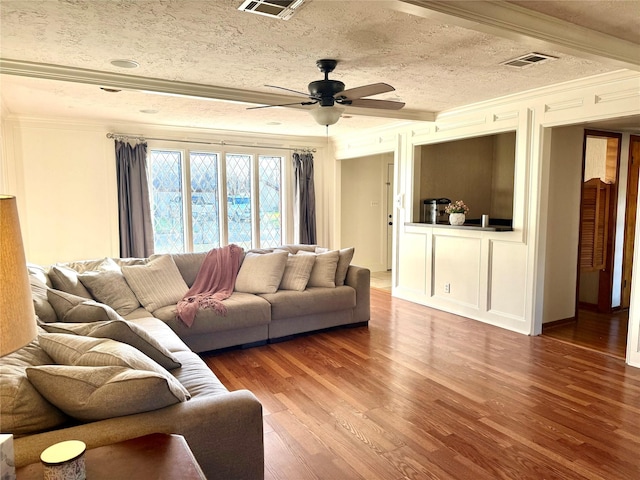 living area featuring visible vents, wood finished floors, a textured ceiling, and ornamental molding