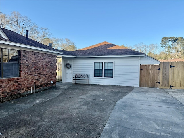 exterior space featuring brick siding, a shingled roof, a gate, and fence