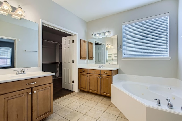 full bathroom with tile patterned floors, two vanities, a sink, a jetted tub, and a healthy amount of sunlight