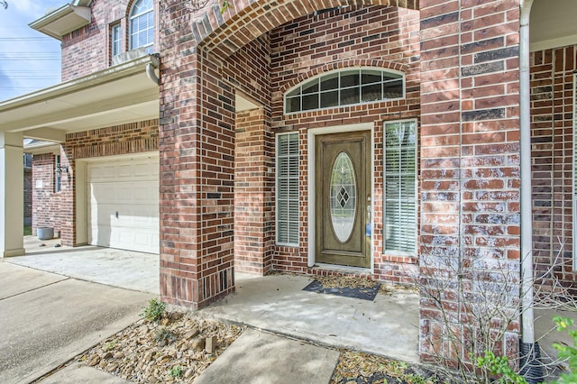 view of exterior entry with brick siding, a garage, and driveway