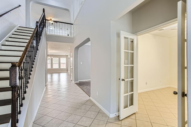 foyer entrance with light tile patterned flooring, stairway, arched walkways, and a towering ceiling