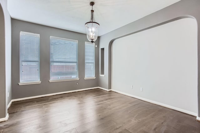 spare room featuring arched walkways, a healthy amount of sunlight, baseboards, and wood finished floors