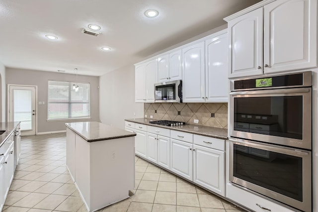 kitchen featuring a center island, white cabinetry, stainless steel appliances, light tile patterned flooring, and decorative backsplash