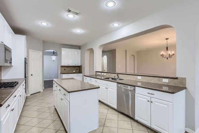 kitchen featuring tasteful backsplash, a center island, appliances with stainless steel finishes, arched walkways, and a sink