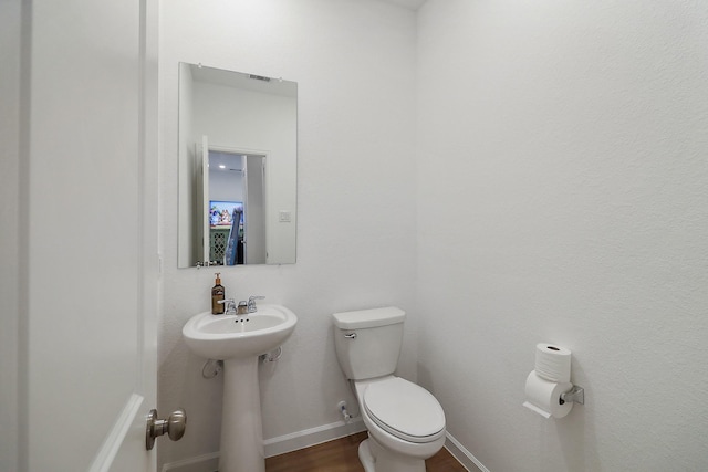 half bath with a sink, toilet, baseboards, and wood finished floors