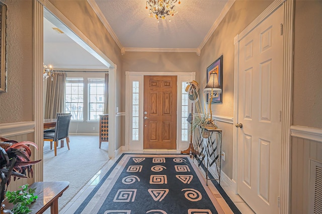 foyer featuring a chandelier, a wainscoted wall, ornamental molding, a textured wall, and a textured ceiling