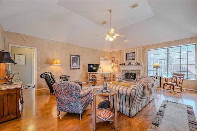 living room with wood finished floors, visible vents, a fireplace with raised hearth, ceiling fan, and vaulted ceiling