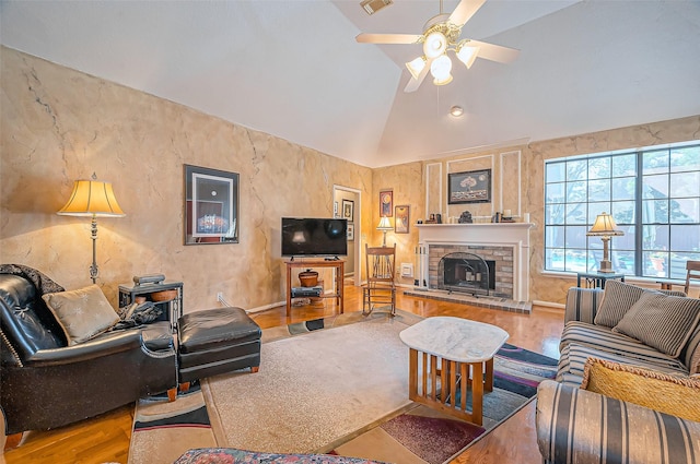 living room featuring a ceiling fan, vaulted ceiling, a brick fireplace, and wood finished floors