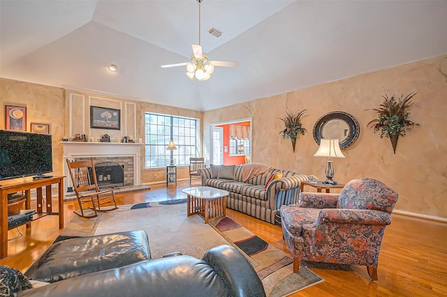 living room with visible vents, a fireplace with raised hearth, a ceiling fan, wood finished floors, and lofted ceiling