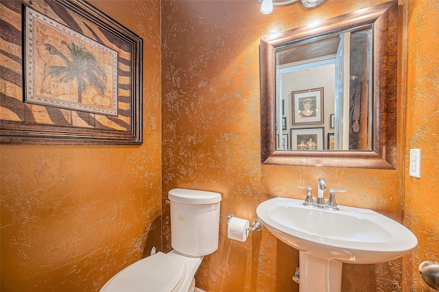 half bath with a sink, toilet, and a textured wall