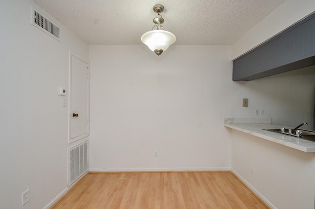 unfurnished dining area featuring a textured ceiling, visible vents, and light wood-type flooring