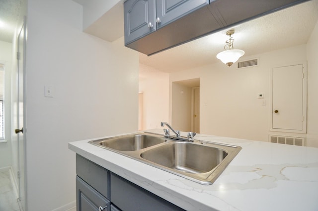 kitchen featuring visible vents, gray cabinetry, pendant lighting, and a sink