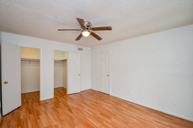 unfurnished bedroom with light wood-style flooring, visible vents, two closets, and a textured ceiling