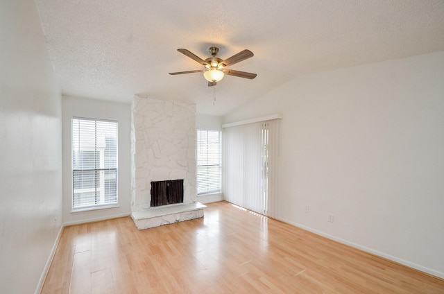 unfurnished living room with a stone fireplace, light wood-type flooring, a wealth of natural light, and a textured ceiling