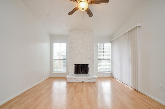 unfurnished living room with a stone fireplace, plenty of natural light, wood finished floors, and a textured ceiling