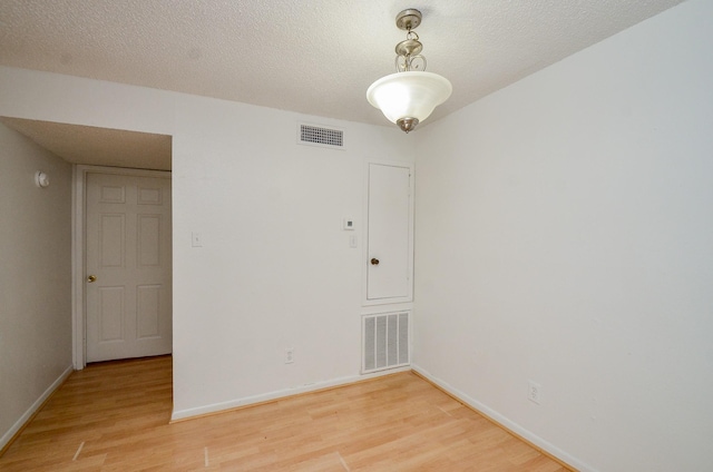 empty room featuring visible vents, light wood-style floors, and a textured ceiling