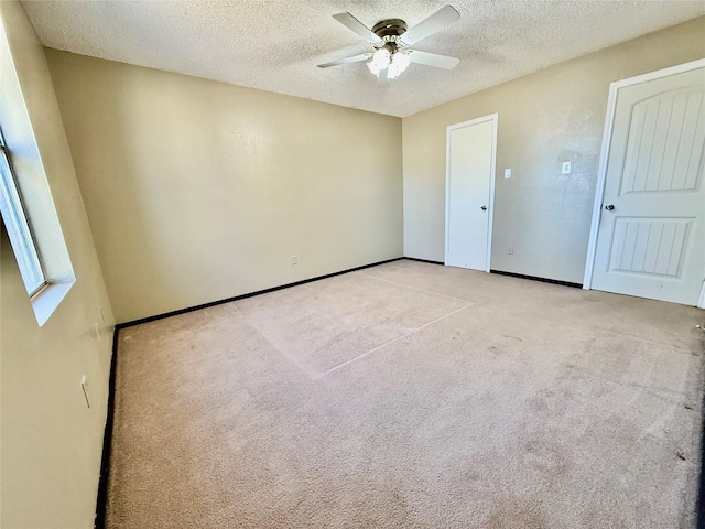 empty room with a textured ceiling, ceiling fan, baseboards, and light carpet