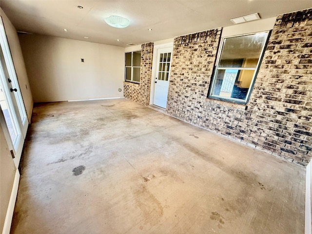 unfurnished room featuring unfinished concrete floors and brick wall