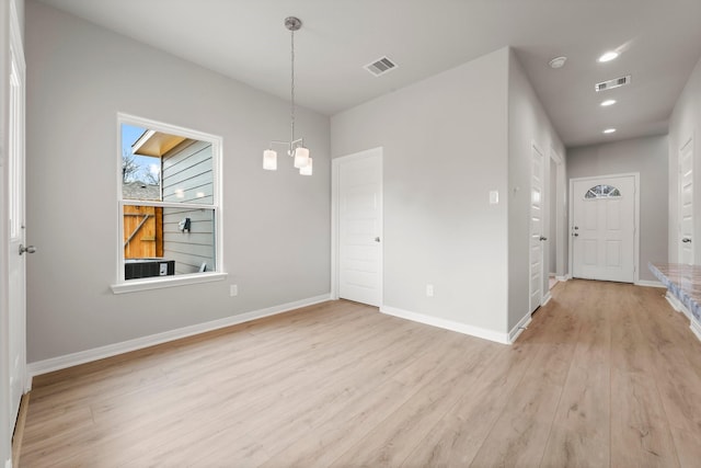 spare room with a notable chandelier, visible vents, light wood-type flooring, and baseboards