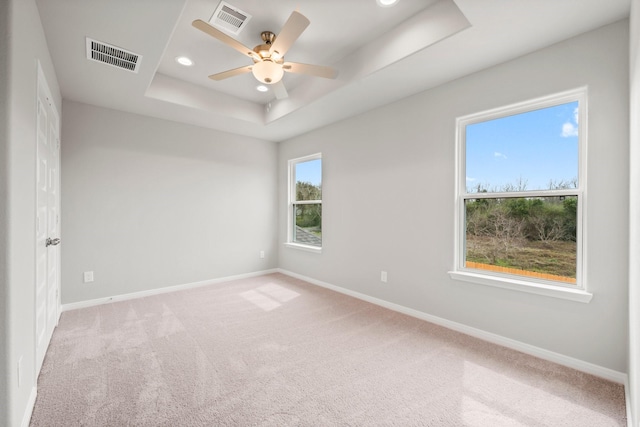 carpeted empty room featuring a tray ceiling, recessed lighting, baseboards, and visible vents