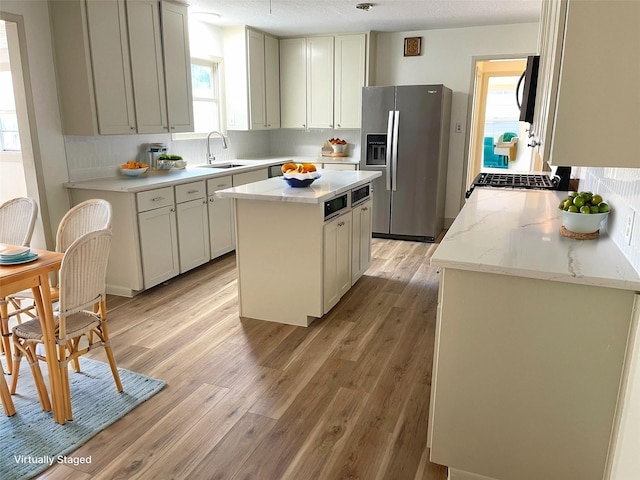 kitchen with stainless steel fridge with ice dispenser, a sink, black microwave, a kitchen island, and light wood-style flooring