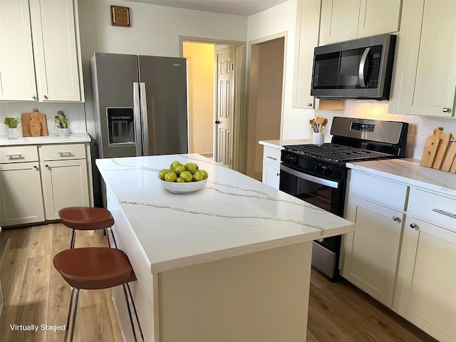 kitchen featuring light stone counters, wood finished floors, a kitchen island, tasteful backsplash, and appliances with stainless steel finishes