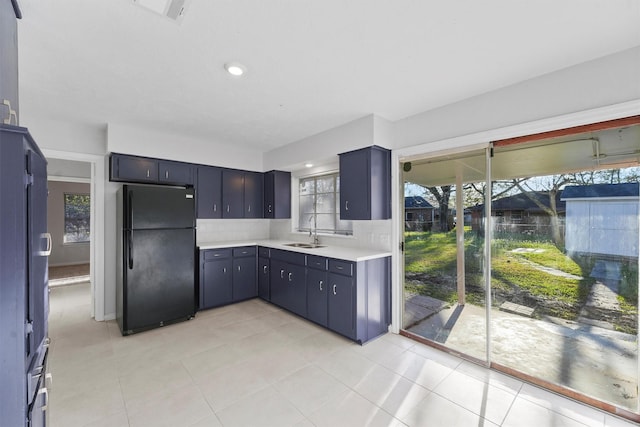 kitchen featuring light countertops, light tile patterned floors, freestanding refrigerator, and a sink