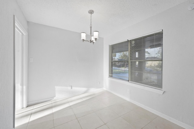 tiled empty room featuring baseboards, a textured ceiling, and an inviting chandelier