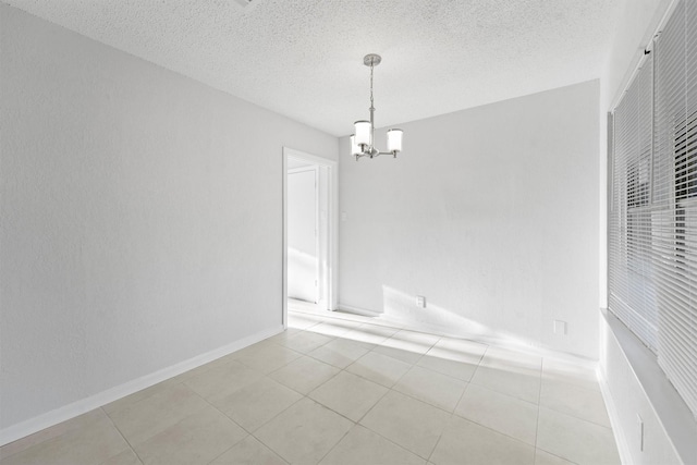 spare room featuring a chandelier, light tile patterned floors, a textured ceiling, and baseboards