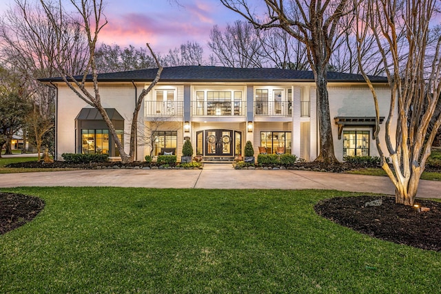 view of front facade featuring brick siding, french doors, a balcony, and a front yard