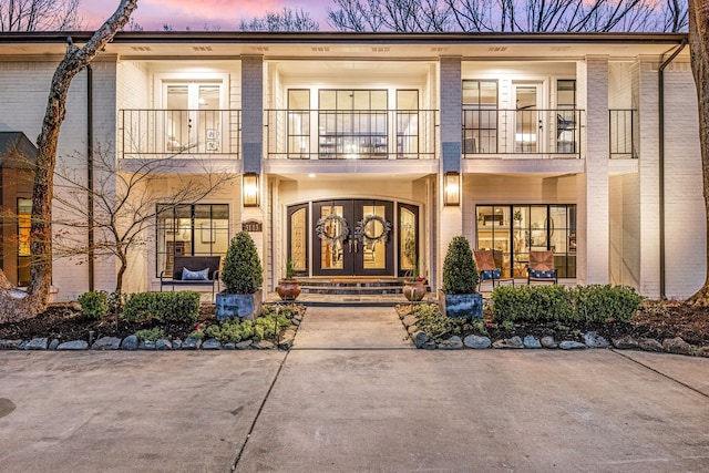 exterior entry at dusk with brick siding, a balcony, and french doors